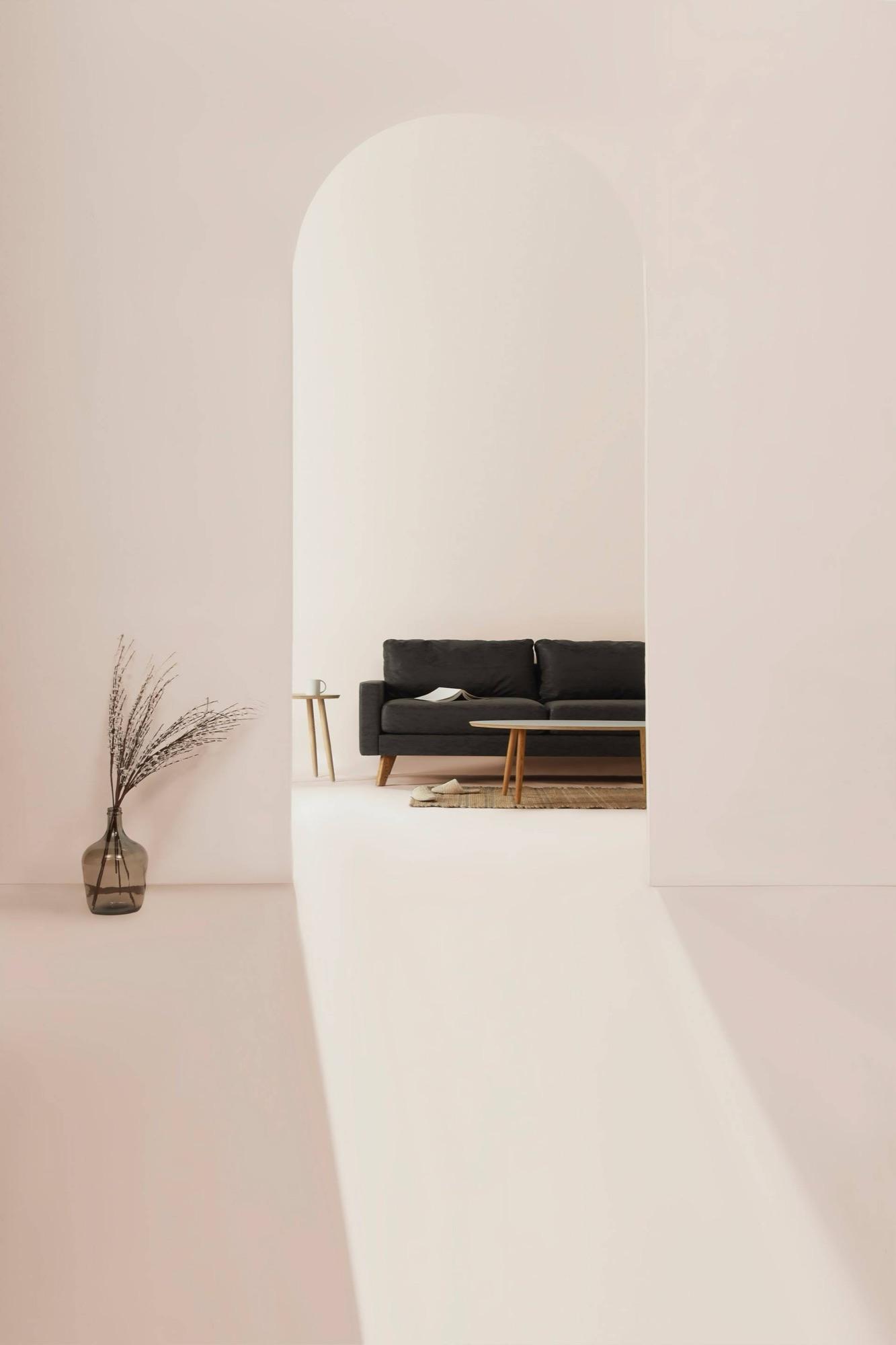 Minimal stone interior with an arched alcove, dark sofa, and dried grasses